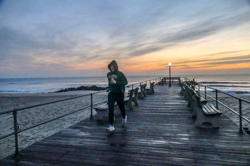 A person is running on a pier near the ocean at sunset.