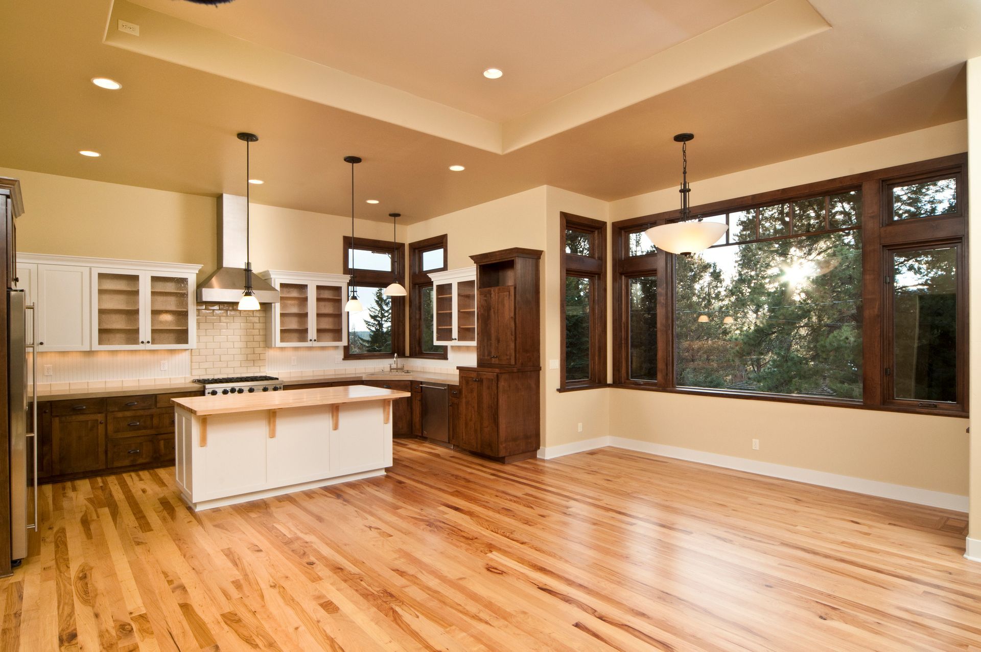 Light hardwood flooring adds warmth to a bright kitchen with white cabinets and large windows.