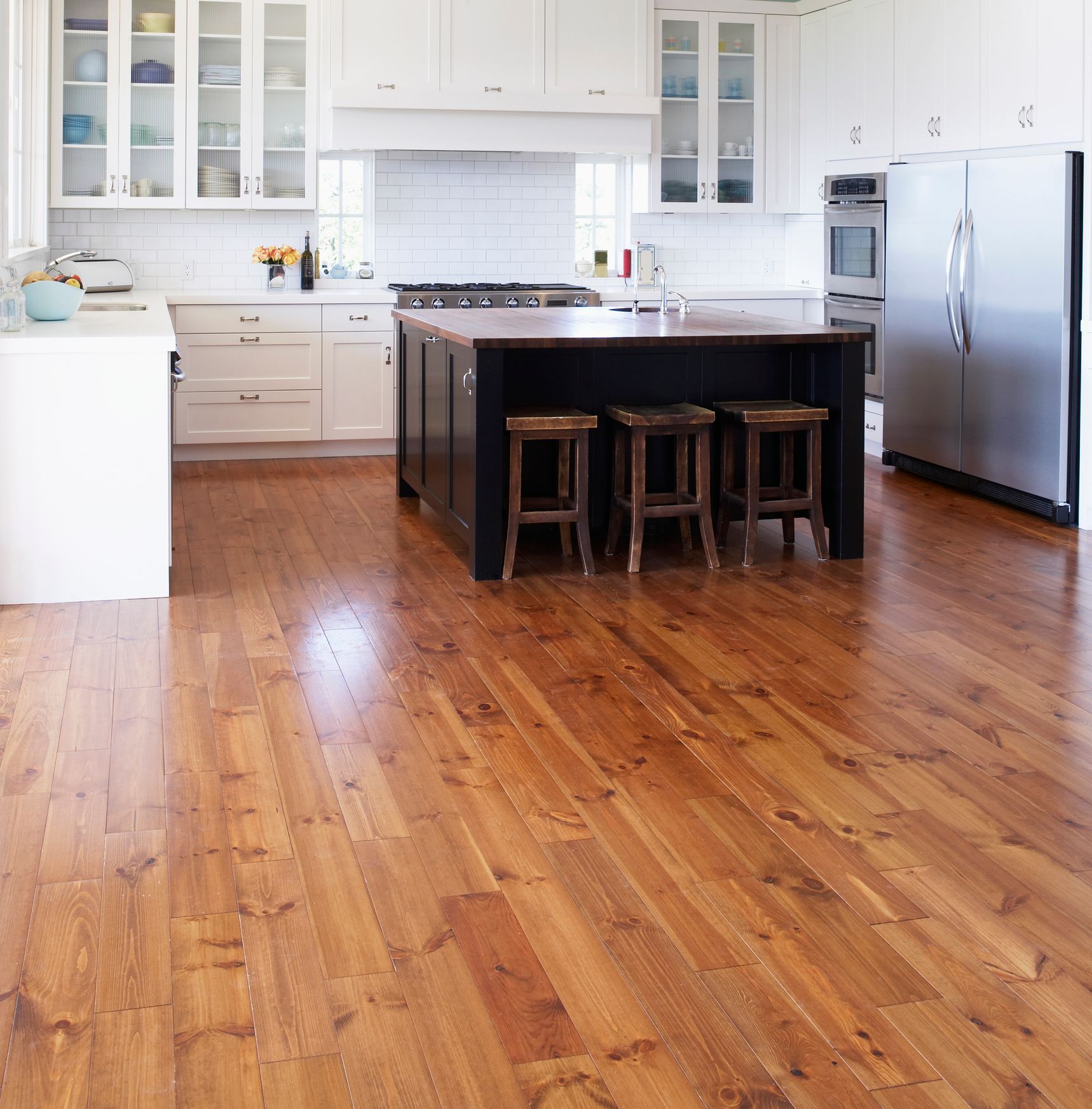Medium-tone hardwood flooring adds warmth to a bright kitchen with white cabinets and island.