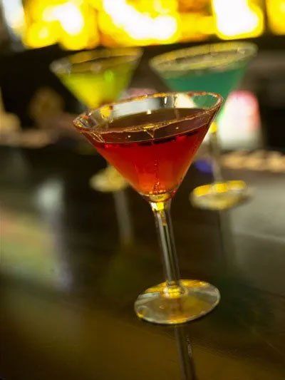 A martini glass filled with a red liquid is sitting on a bar.