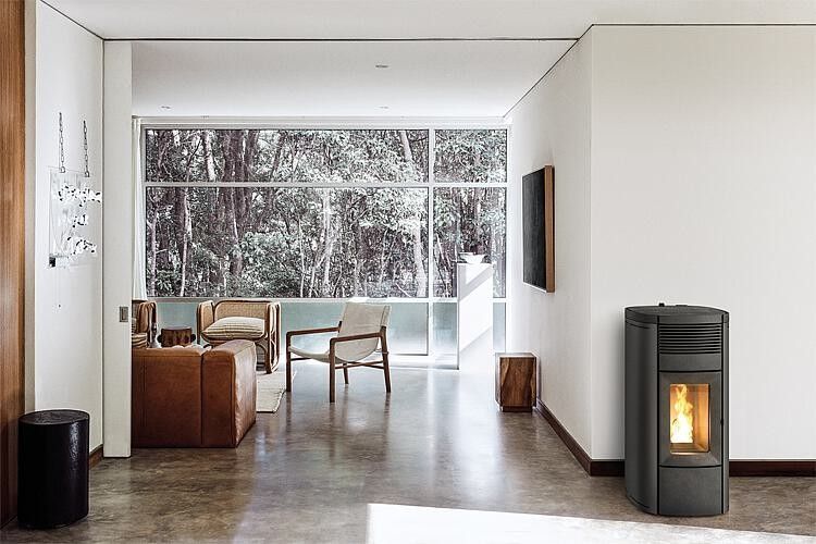 Soggiorno moderno con stufa a pellet, ampie finestre e mobili dai toni neutri con vista sulla foresta.