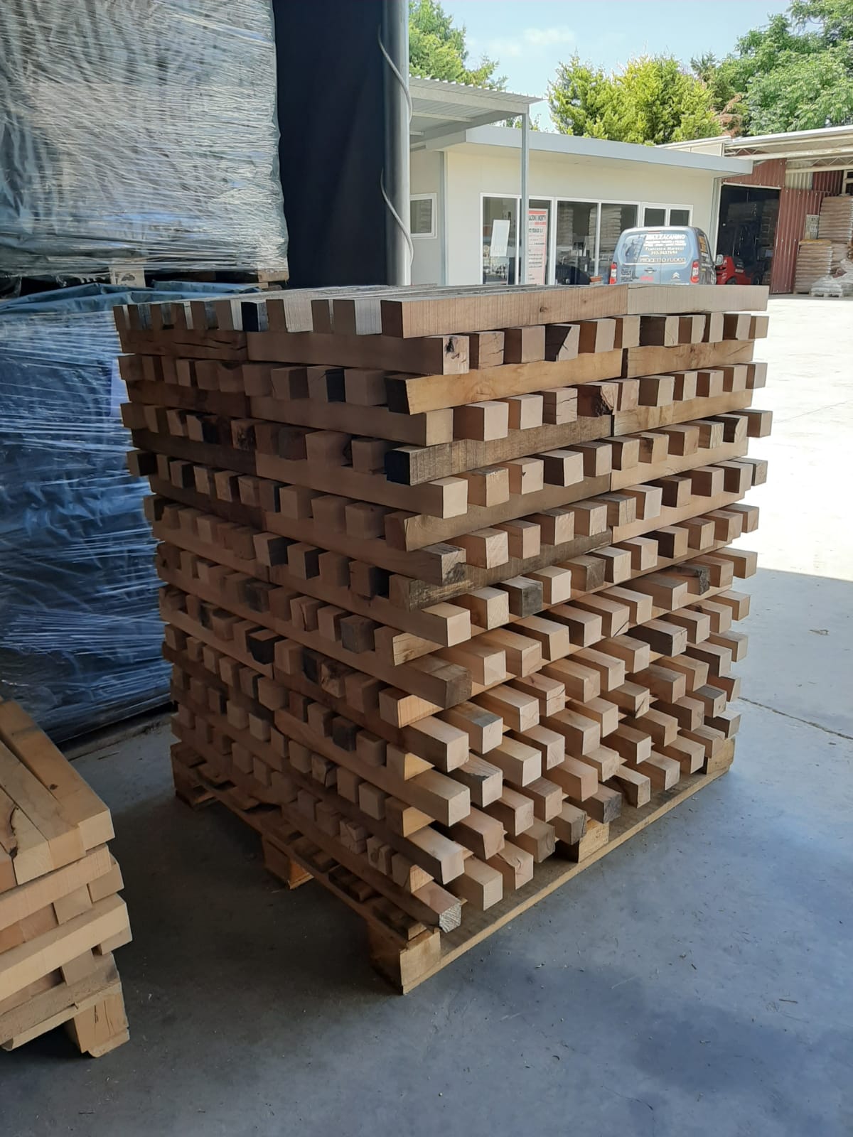 Pila di assi di legno su un pallet, all'aperto, vicino a un edificio.