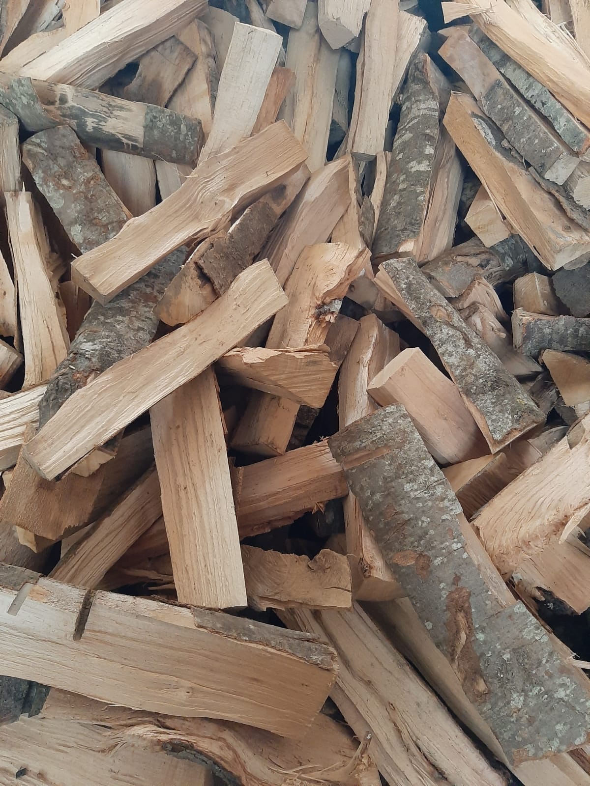 Catasta di tronchi di legna da ardere spaccati con corteccia.