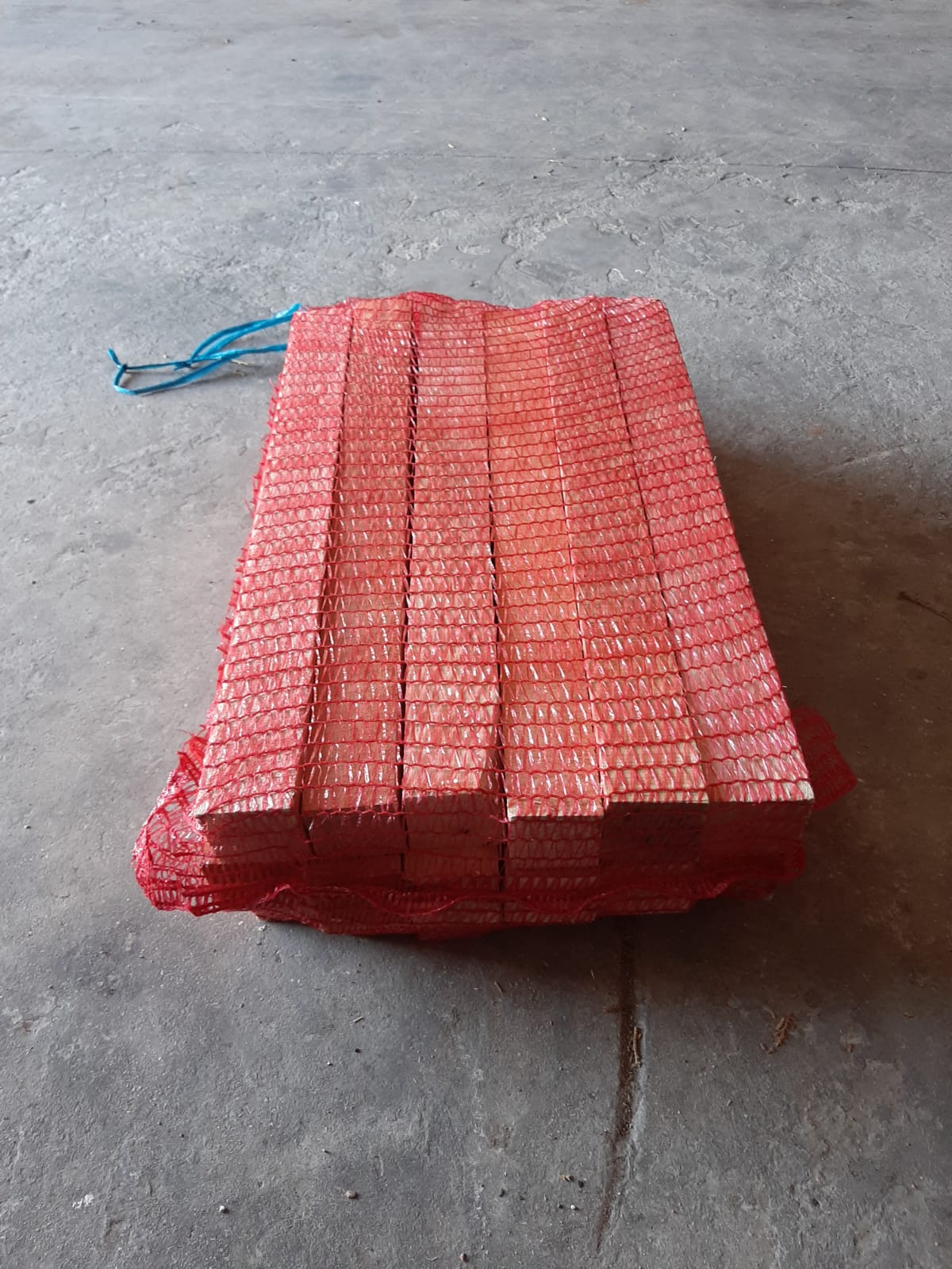 Sacco di blocchi di legno rossi, rettangolari, impilati su una superficie di cemento grigio.