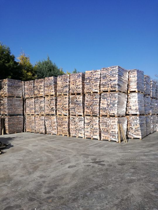 Cataste di pallet di legno avvolti in plastica trasparente contro un cielo azzurro.