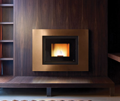 Moderno camino con cornice in rame, incassato in una parete rivestita in legno. Fiamme visibili all'interno del focolare.