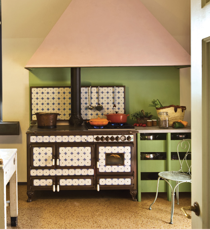 Cucina con grande piano cottura, pareti verdi, cappa rosa e dettagli piastrellati.