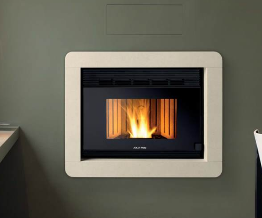 Una stufa a pellet montata a parete con fuoco acceso, circondata da una cornice color crema su una parete verde.