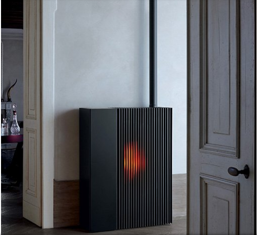 Stufa a pellet moderna nera con fiamma accesa, contro una parete bianca, vicino a una porta.