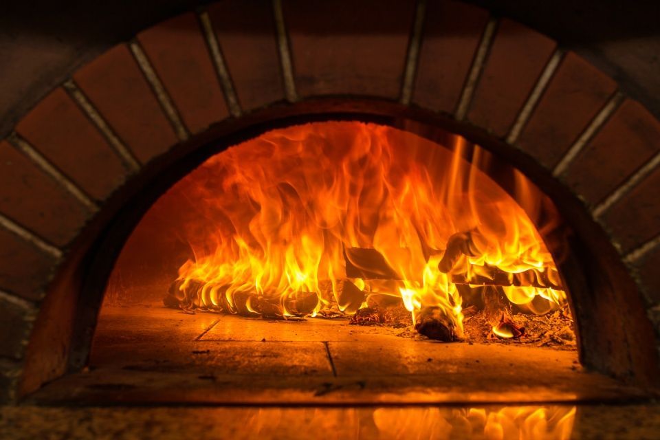 Forno di mattoni in fiamme con legna che arde, le cui fiamme emanano una luce arancione e gialla brillante.
