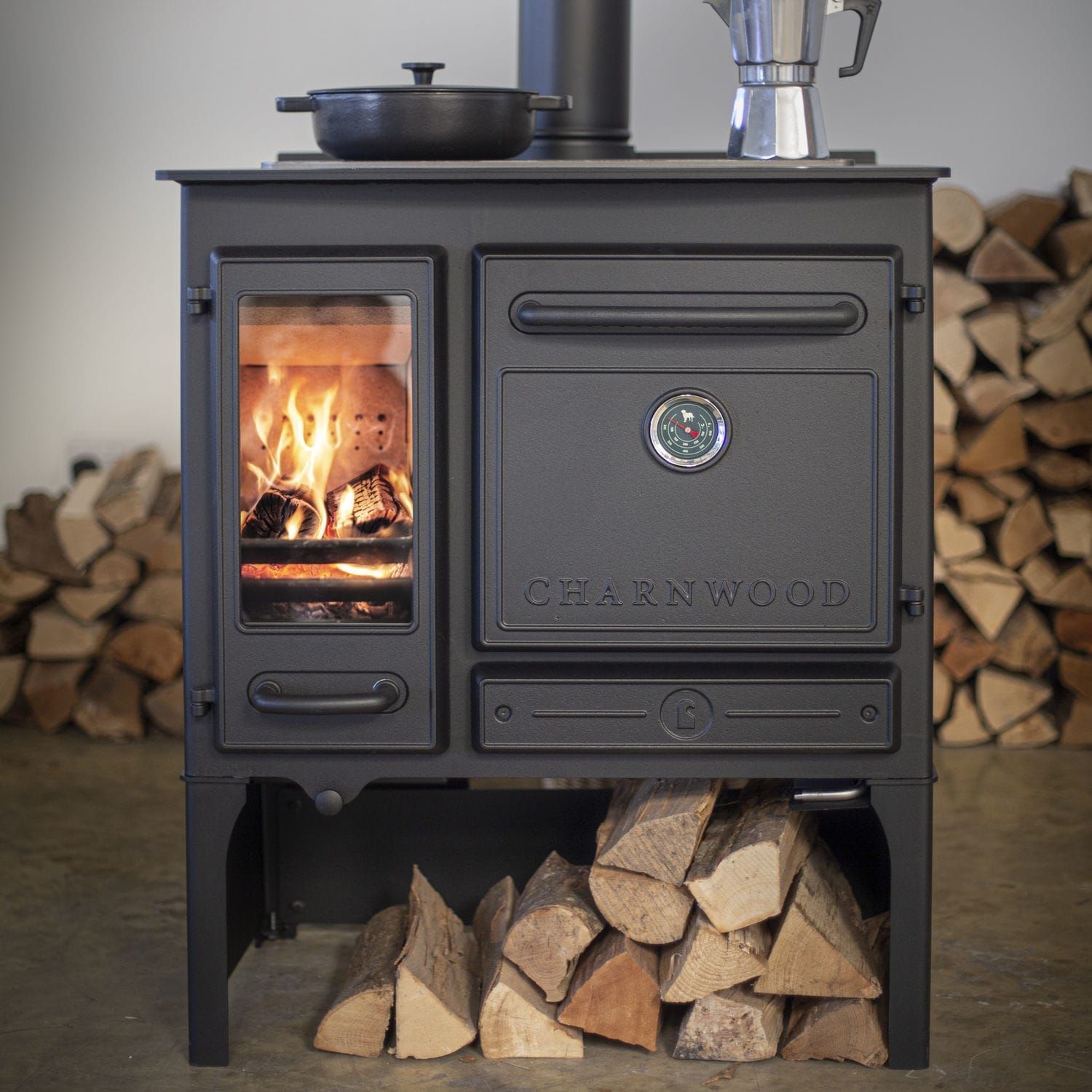 Una stufa a legna nera con fuoco acceso e legna da ardere, all'interno di una stanza.