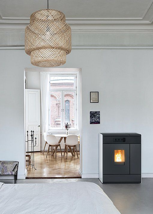 Moderna stufa a pellet in una stanza con pareti bianche; una porta aperta conduce alla zona pranzo con tavolo e sedie.