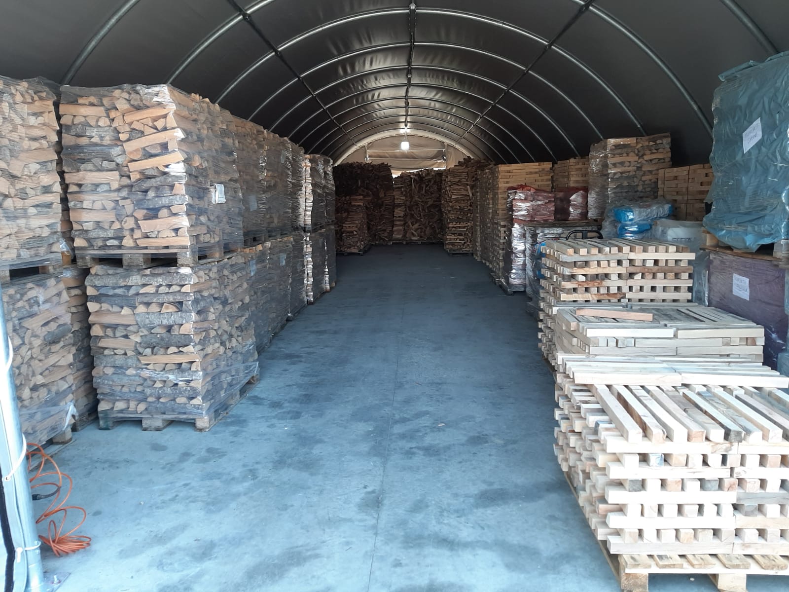 Pile di pallet di legno carichi di materiali all'interno di una lunga struttura industriale ad arco.