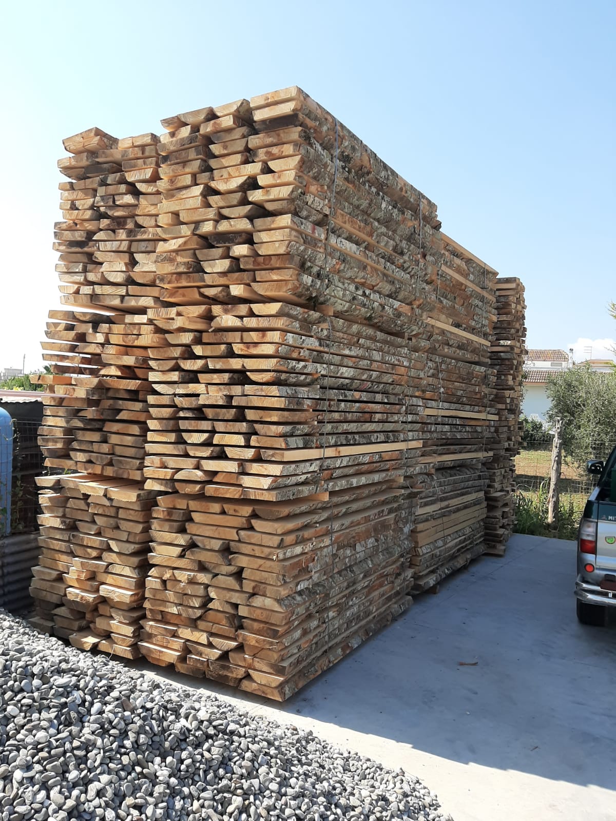Grande pila di assi di legno su una superficie di cemento sotto un cielo terso e azzurro.