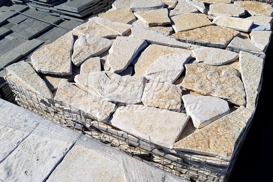 Fasci impilati di piastrelle irregolari di pietra chiara, probabilmente per uso paesaggistico.