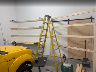 Garage with yellow step ladder, shelving under construction, and a yellow truck.