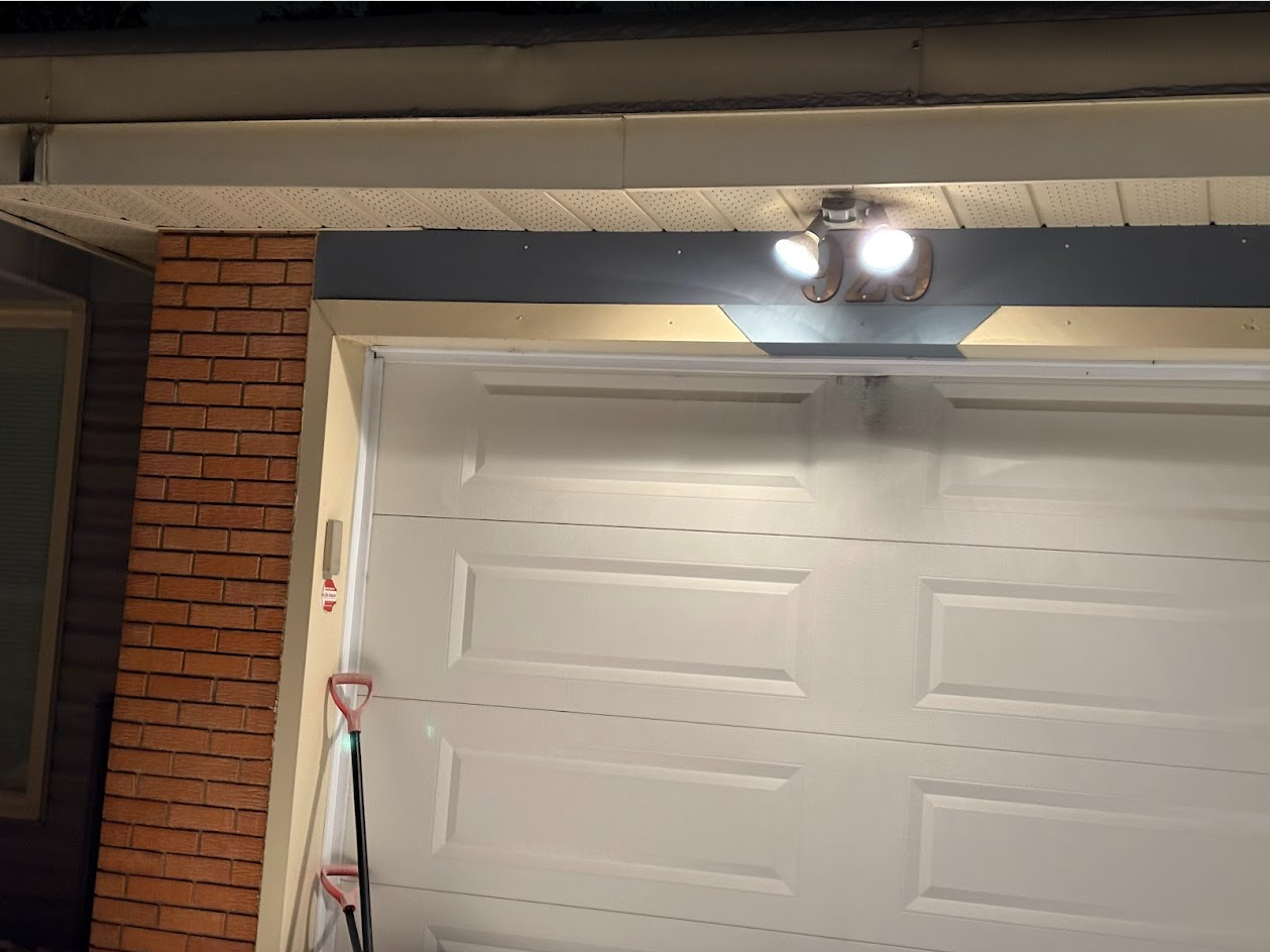 White garage door under a light fixture, next to a brick wall.