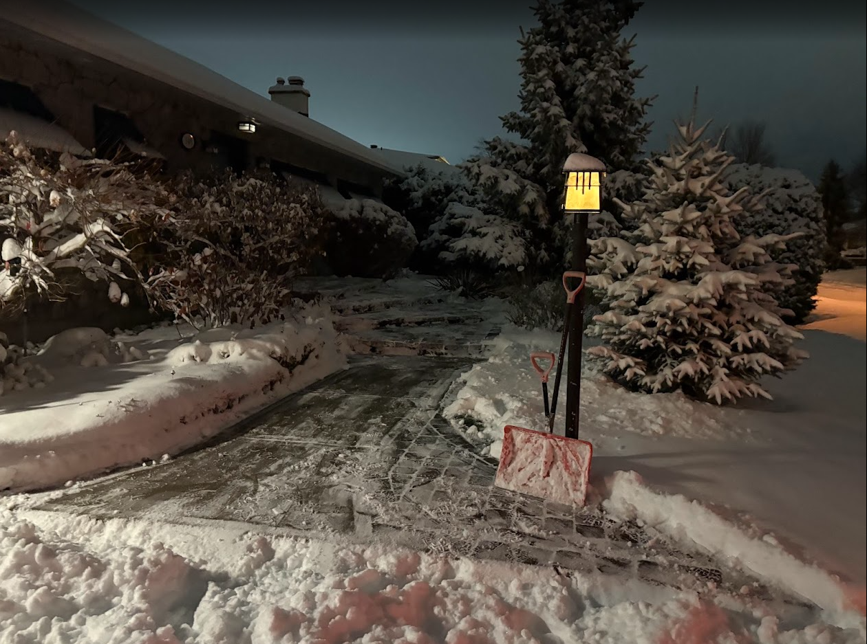 Snow-covered brick walkway and steps at night. Partially cleared path and piled snow on sides.