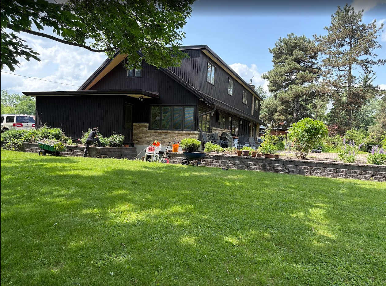 Black house with stone facade, green lawn, garden beds, and cloudy sky.
