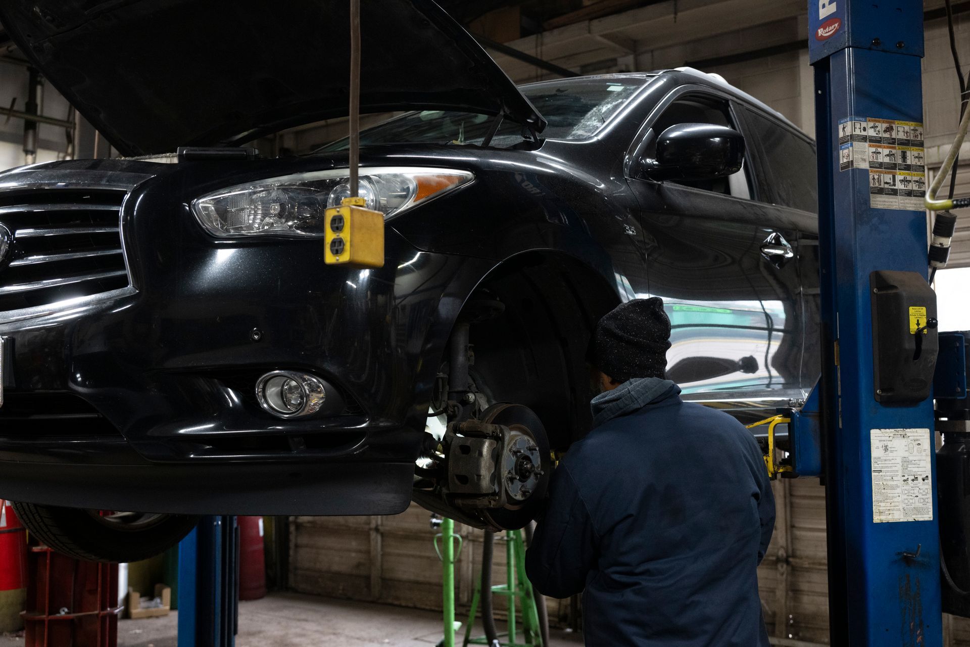 A man is working on a car on a lift in a garage. | Meineke Car Care Center