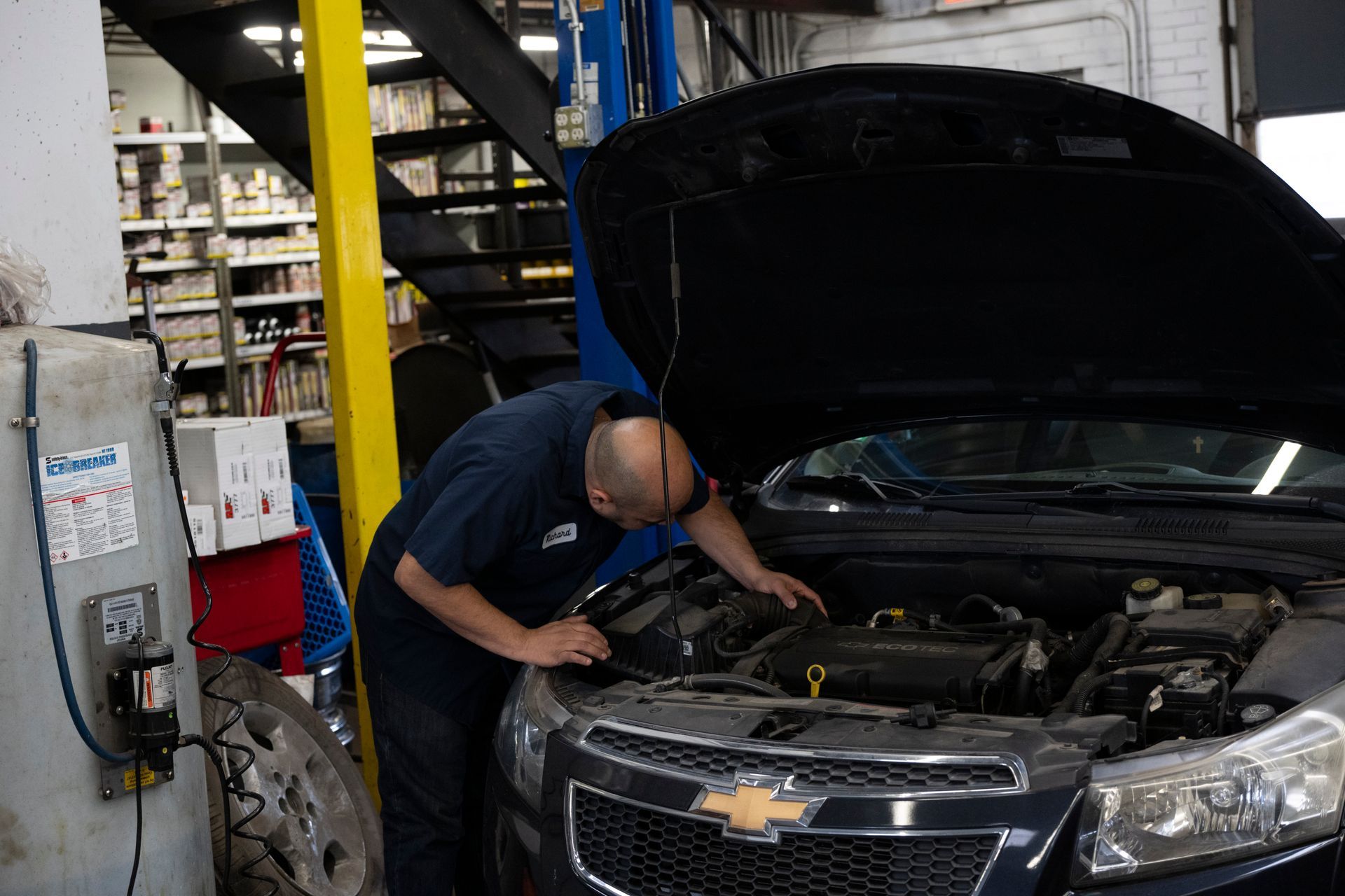 A man is looking under the hood of a car in a garage. | Meineke Car Care Center