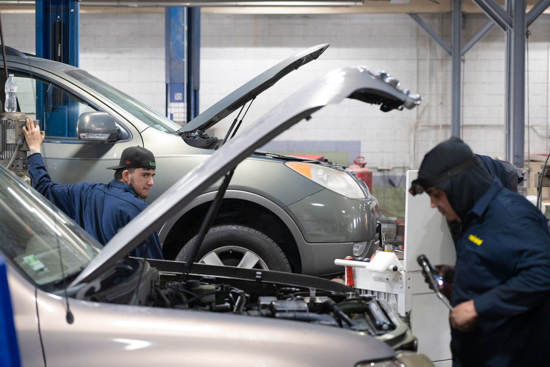 Two mechanics are working on a car in a garage with the hood up. | Meineke Car Care Center