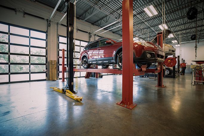 A red car is sitting on a lift in a garage. | Meineke Car Care Center