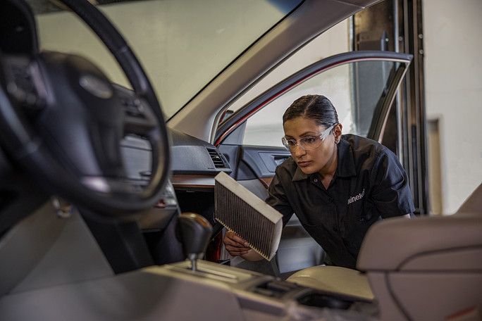 A woman is cleaning the air filter in a car. | Meineke Car Care Center