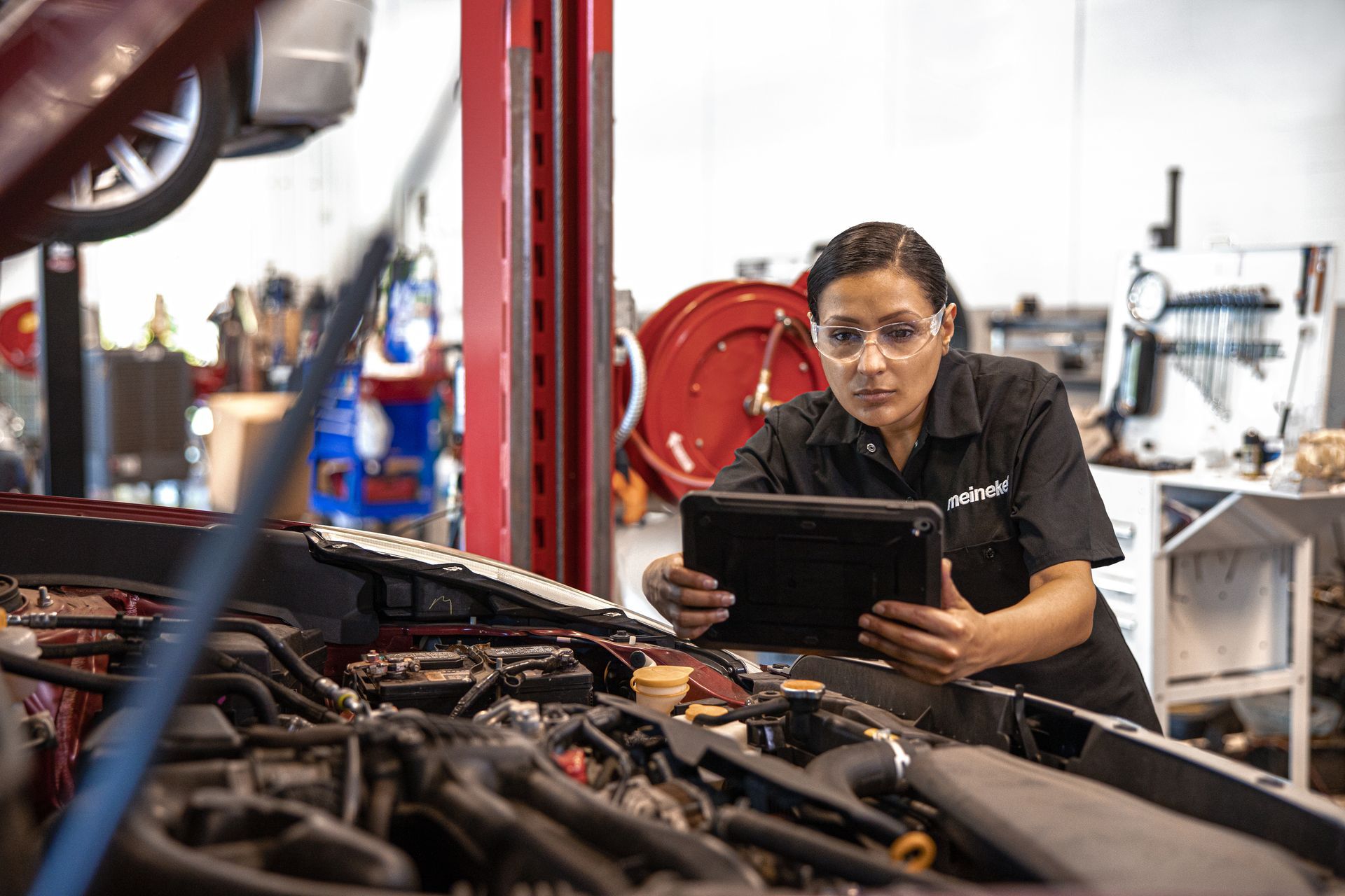 A woman is looking at a tablet while working on a car in a garage. | Meineke Car Care Center