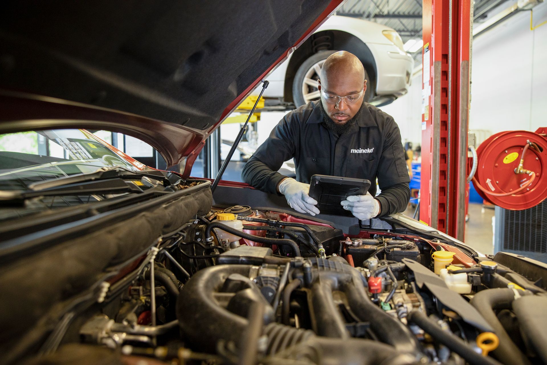 A man is working on the engine of a car in a garage. | Meineke Car Care Center