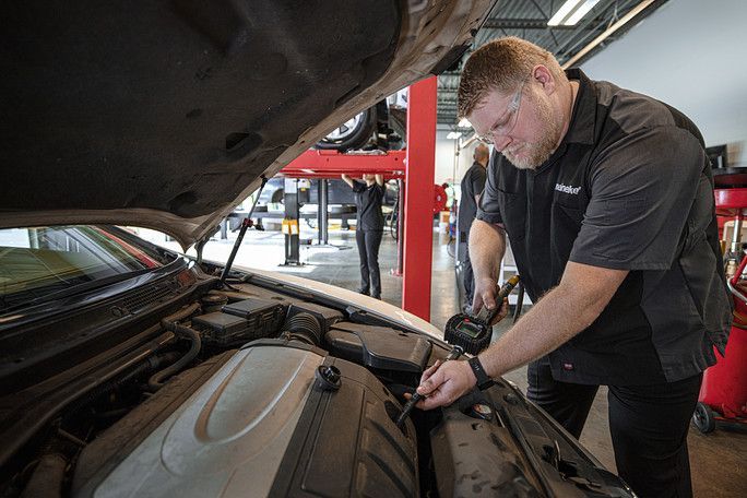 A man is working under the hood of a car in a garage. | Meineke Car Care Center