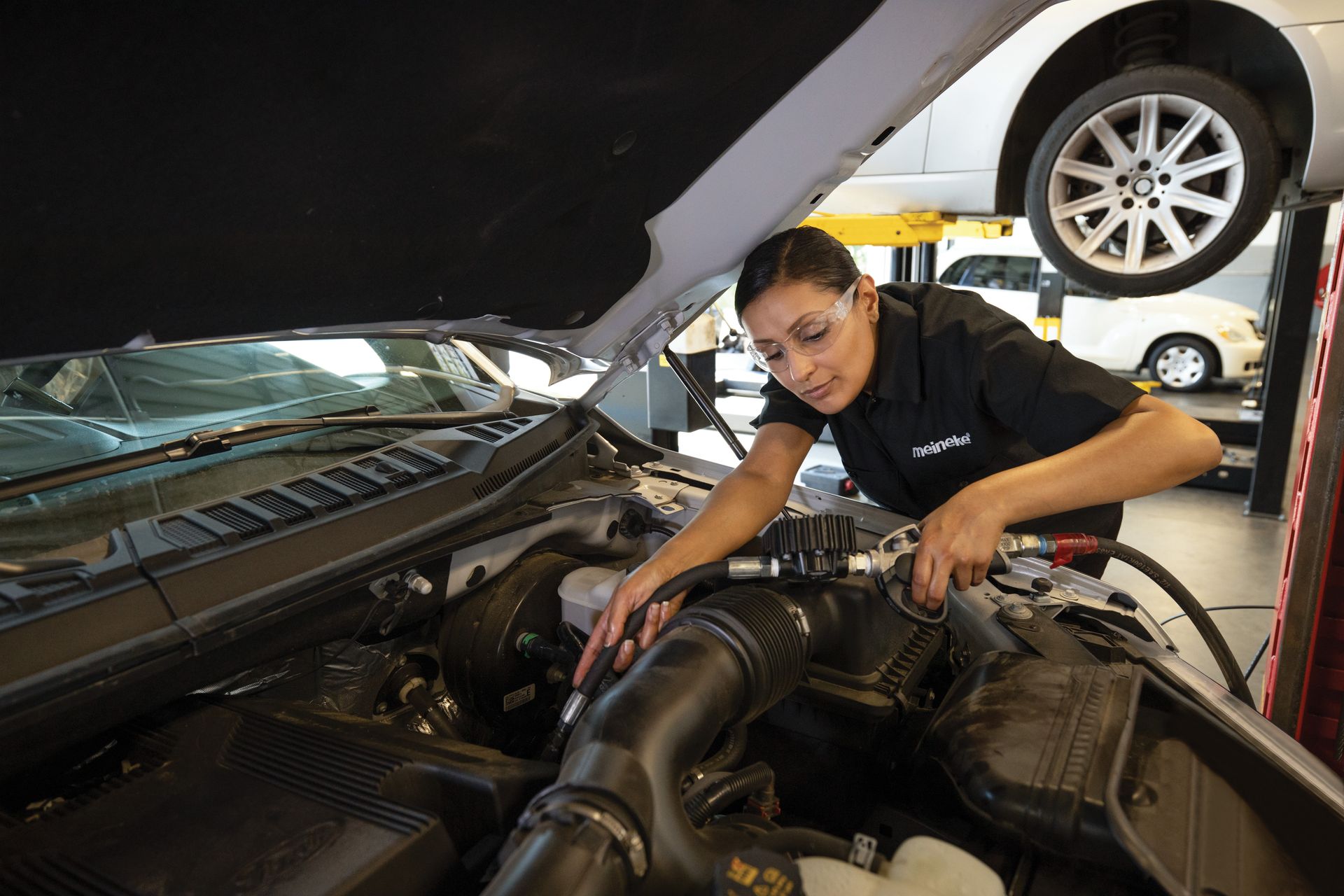 A woman is working on the engine of a car. | Meineke Car Care Center