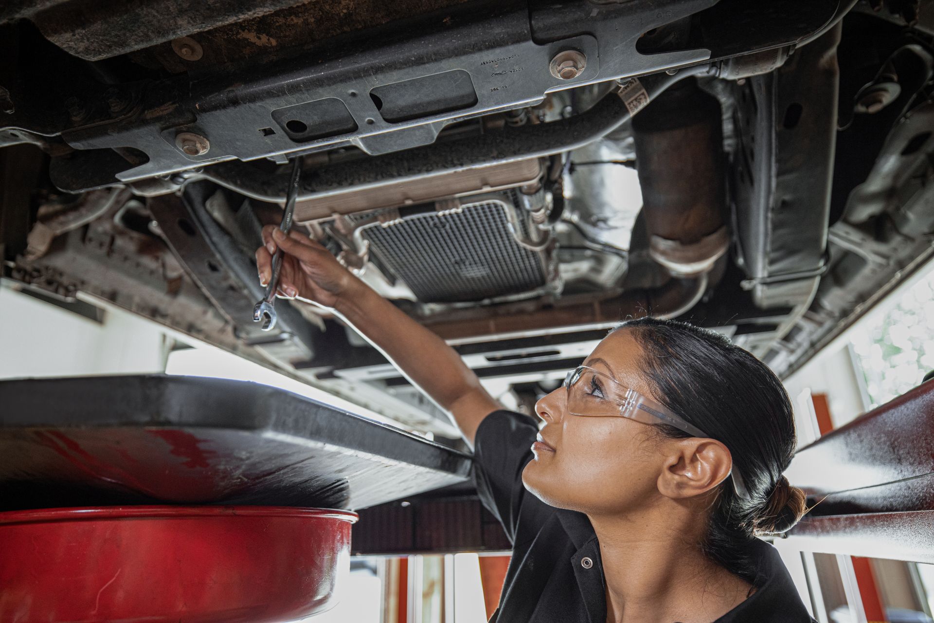 A woman is working underneath a car in a garage. | Meineke Car Care Center