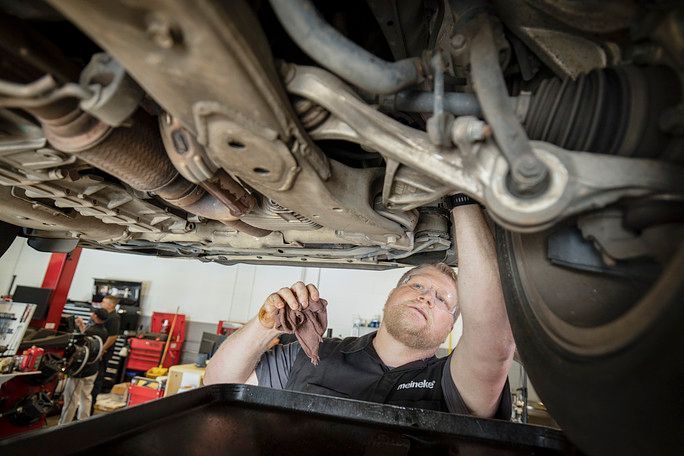 A man is working under a car in a garage. | Meineke Car Care Center