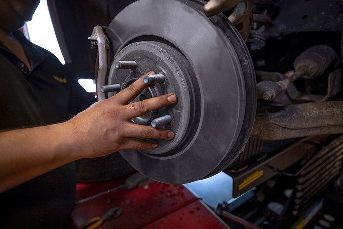 A man is fixing a brake disc on a car. | Meineke Car Care Center