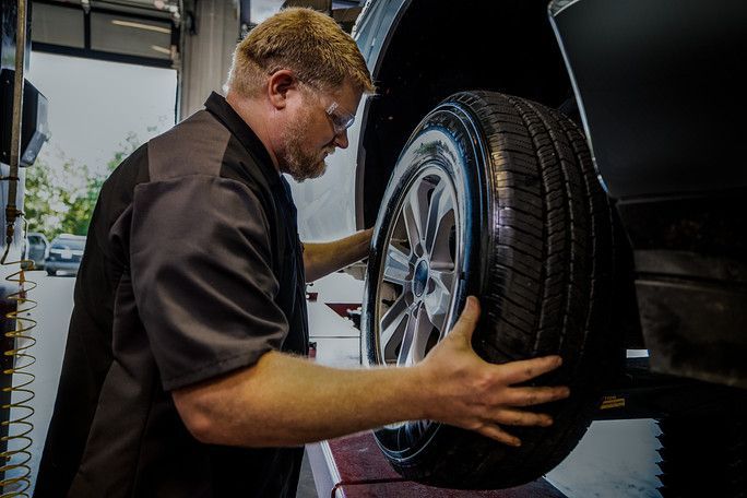 A man is adjusting a tire on a car in a garage. | Meineke Car Care Center