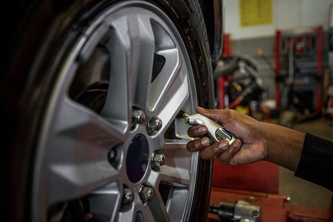 A person is checking the pressure of a tire in a garage. | Meineke Car Care Center