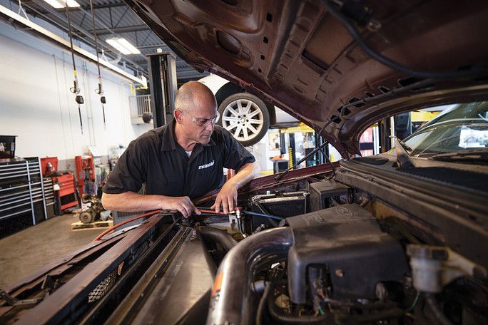 A man is working on the engine of a car in a garage. | Meineke Car Care Center