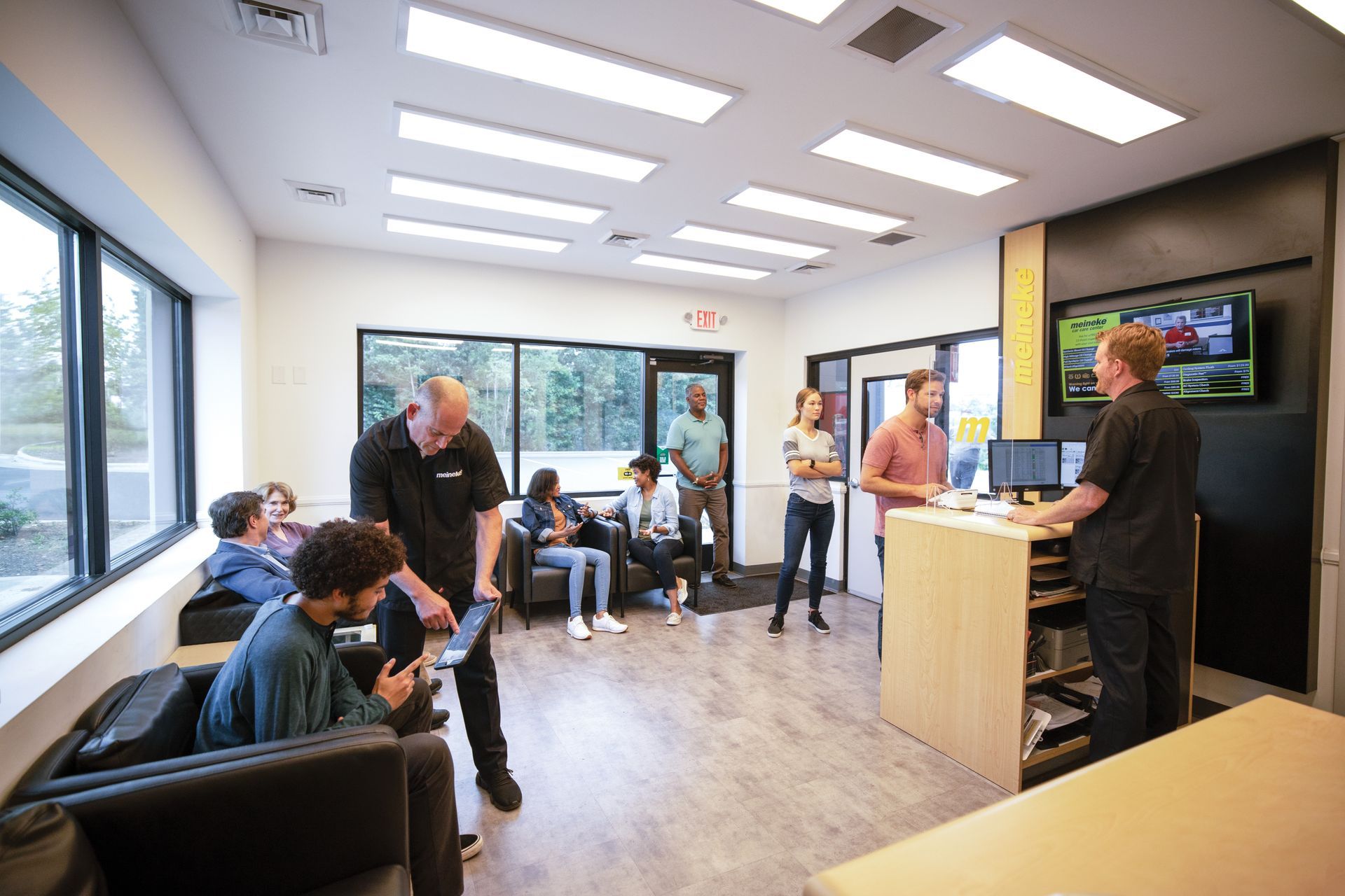 A group of people are standing and sitting in a waiting room. | Meineke Car Care Center