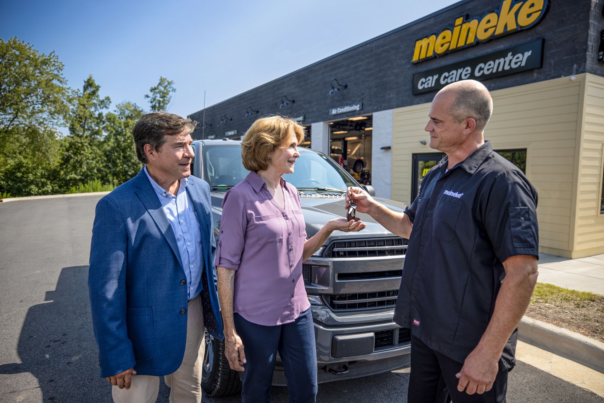 A man is giving a woman a car key in front of a car care center. | Meineke Car Care Center