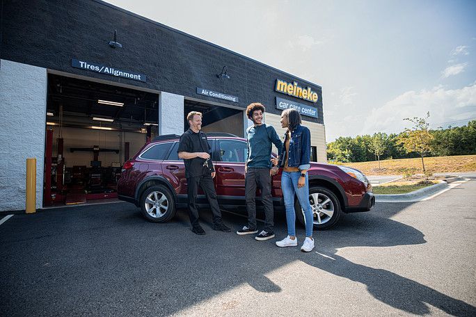A group of people are standing next to a red suv in front of a building. | Meineke Car Care Center