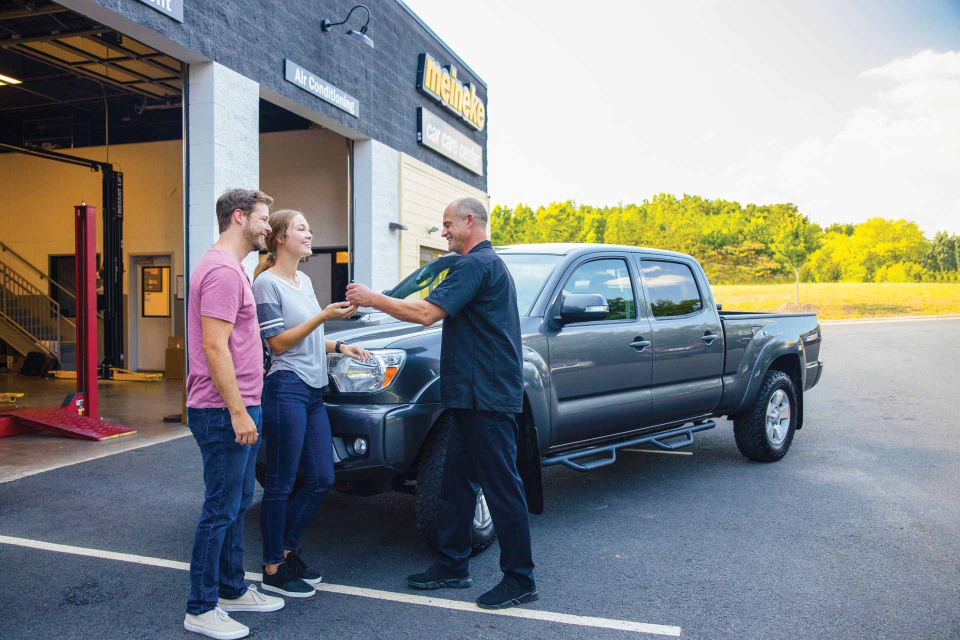 A man is giving a woman a key to a truck. | Meineke Car Care Center
