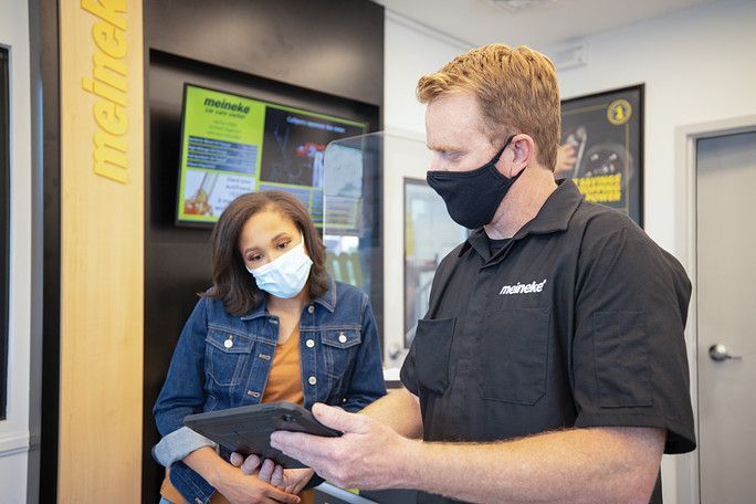 A man and a woman wearing face masks are looking at a tablet. | Meineke Car Care Center