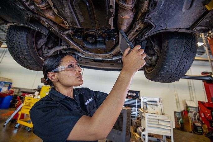 A woman is working under a car in a garage. | Meineke Car Care Center