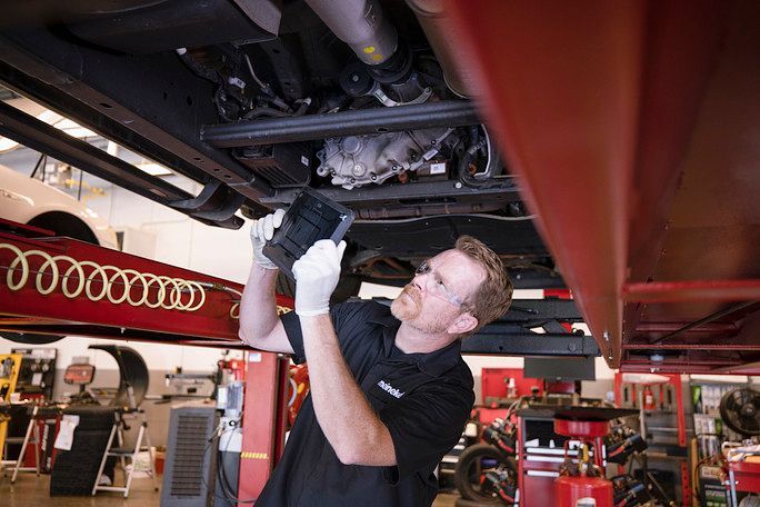 A man is working under a car in a garage. | Meineke Car Care Center