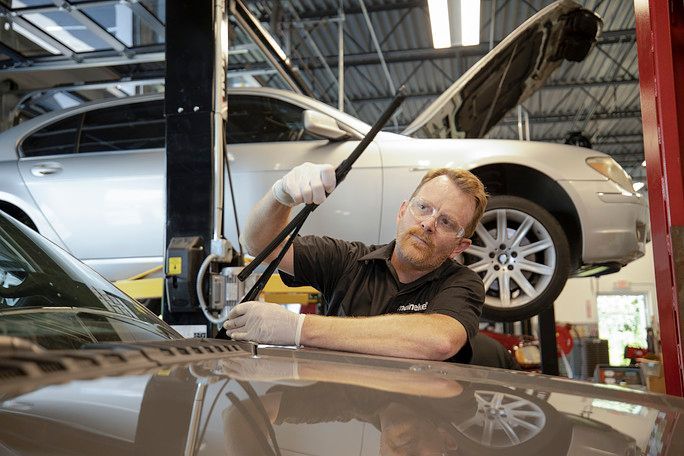 A man is leaning on the hood of a car on a lift. | Meineke Car Care Center