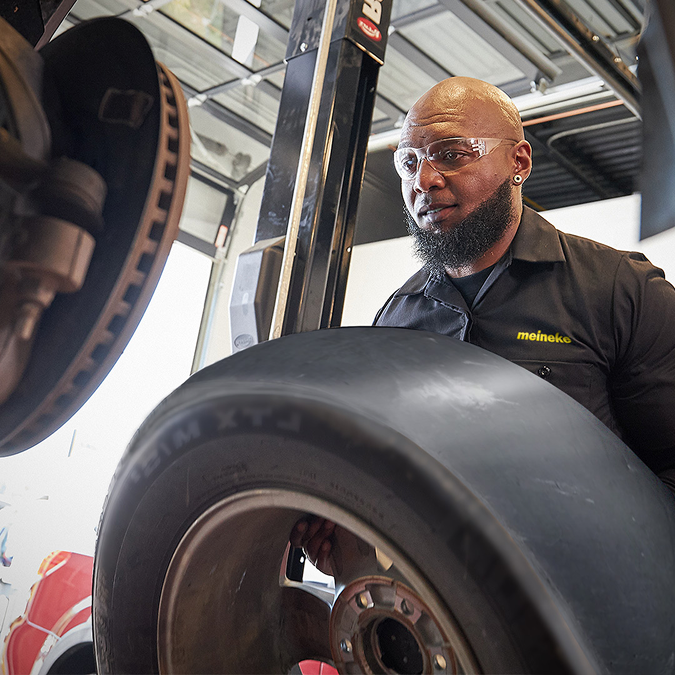 A man wearing glasses is working on a tire | Beacon Auto Repair Center