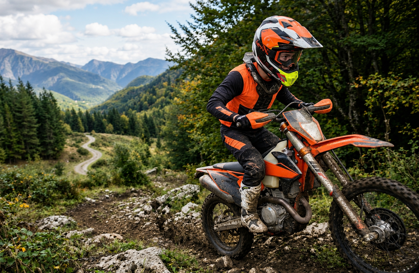 Un motociclista vestito di arancione percorre un sentiero sterrato in una foresta di montagna, con imponenti cime sullo sfondo.