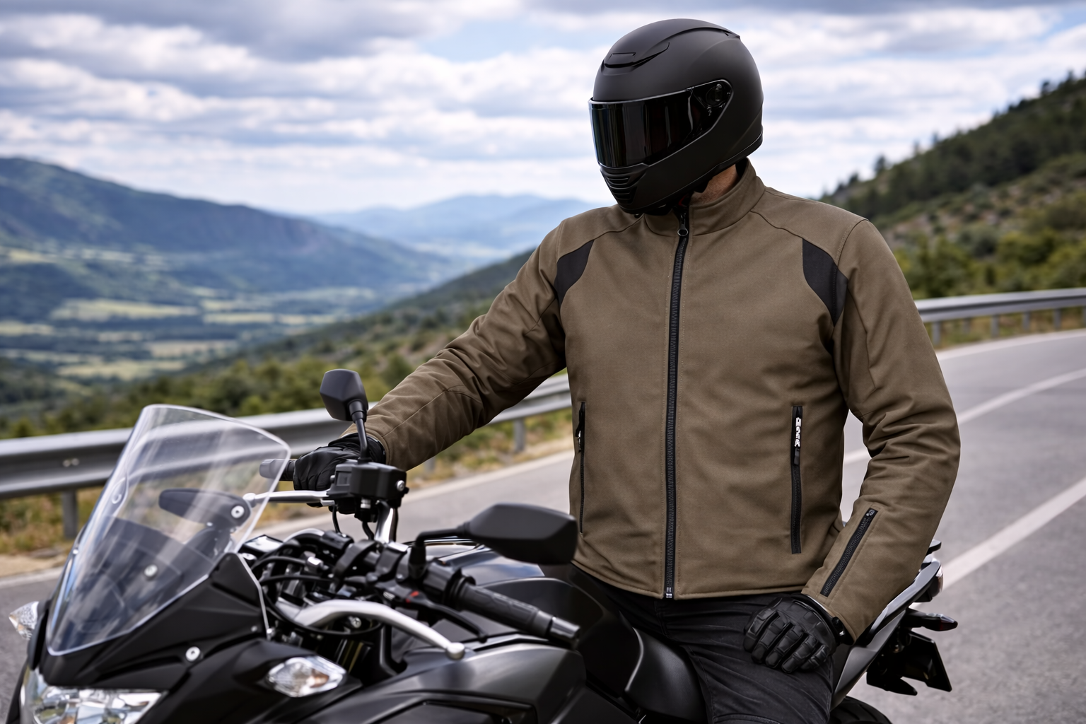 Un motociclista con casco scuro e giacca color cachi è seduto sulla sua motocicletta su una pittoresca strada di montagna.