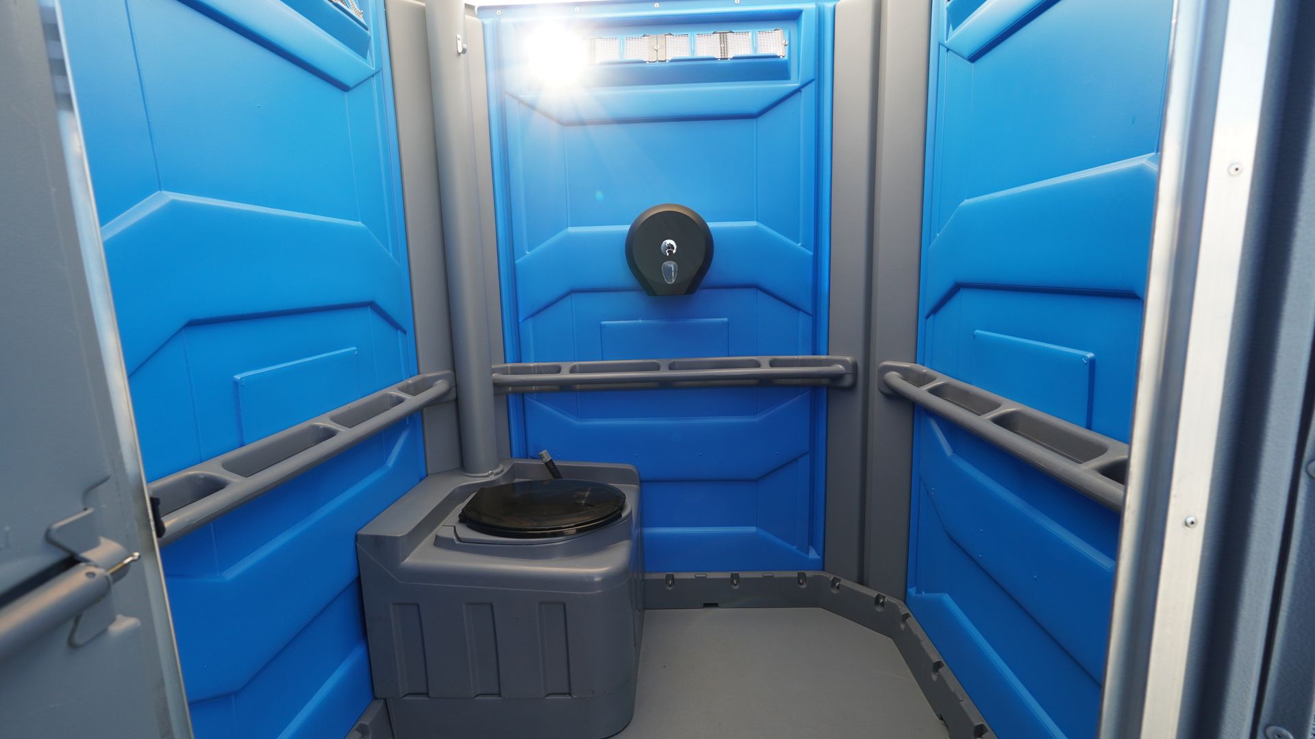 Interior of a blue portable toilet, showing the toilet, walls, and door.